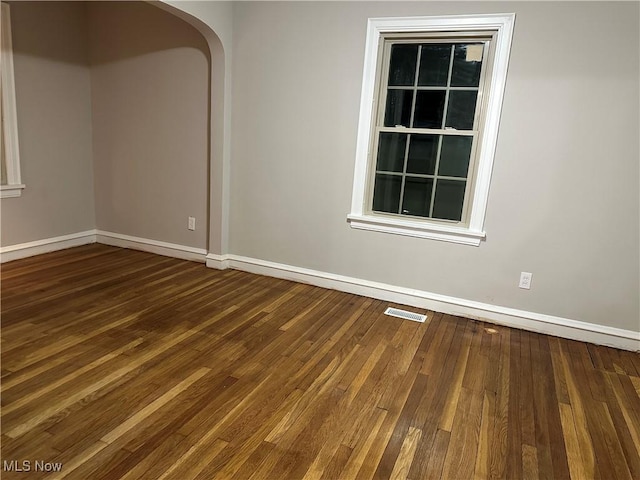 spare room featuring baseboards, visible vents, dark wood finished floors, and arched walkways