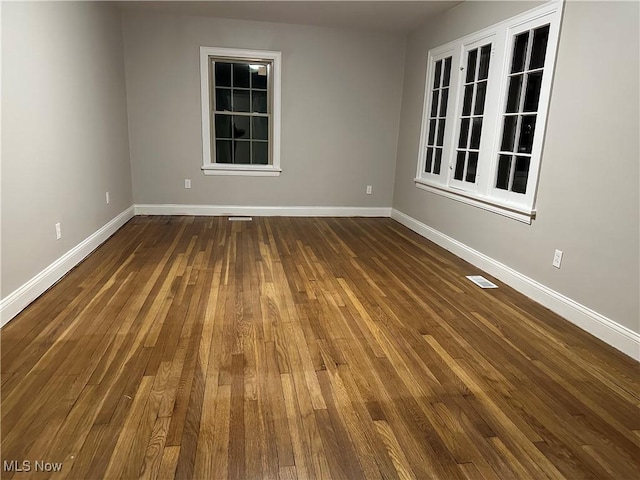 empty room featuring dark wood-style floors, visible vents, and baseboards