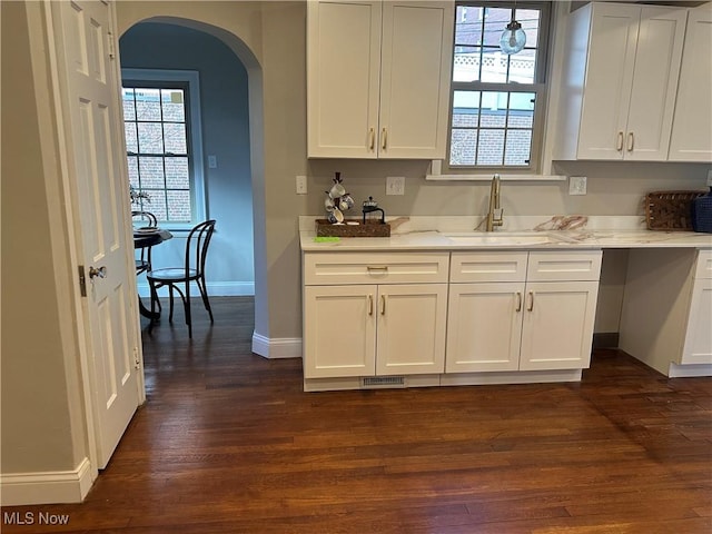 kitchen with arched walkways, dark wood-style flooring, white cabinetry, a sink, and baseboards