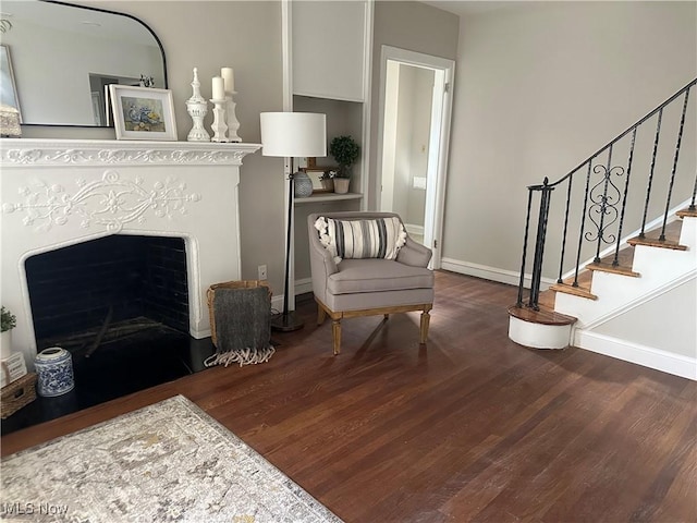 sitting room featuring dark wood-style flooring, a fireplace, stairway, and baseboards