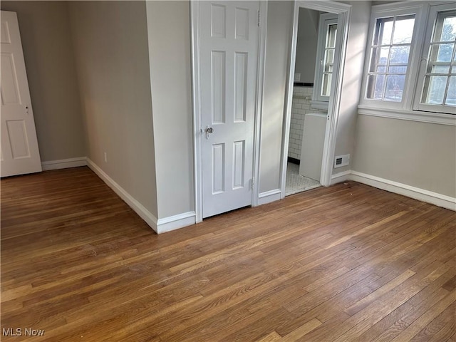 unfurnished bedroom with visible vents, connected bathroom, baseboards, and wood finished floors