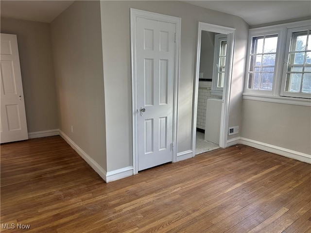 unfurnished bedroom featuring visible vents, connected bathroom, baseboards, and wood finished floors