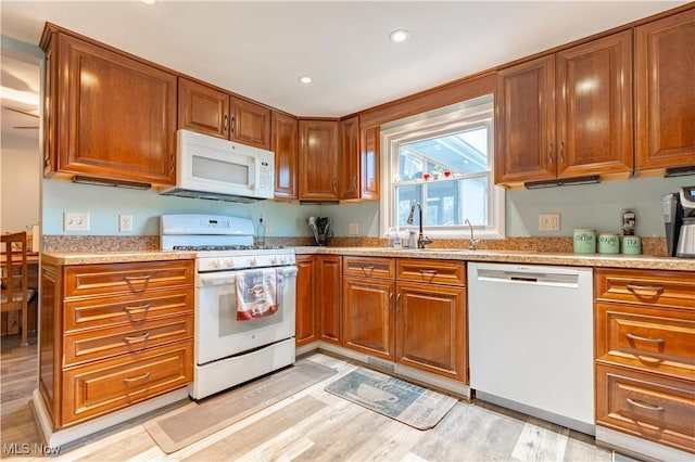 kitchen with sink, light stone counters, white appliances, and light wood-type flooring