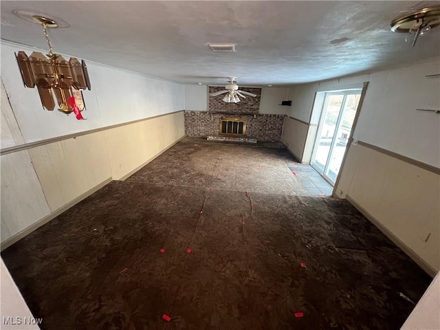 unfurnished living room featuring a brick fireplace and ceiling fan with notable chandelier