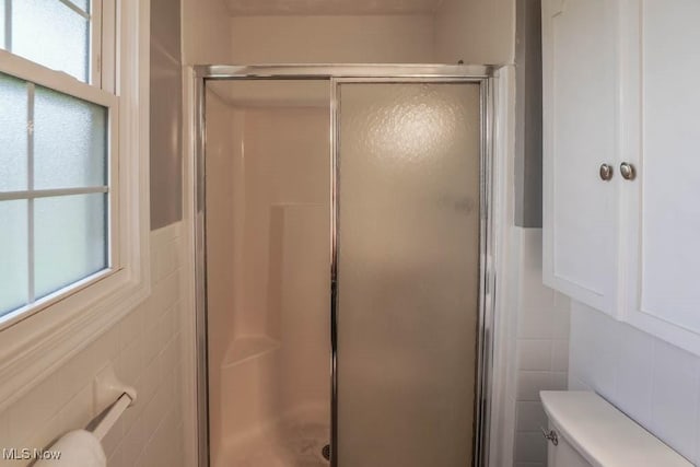 bathroom featuring walk in shower, toilet, and tile walls