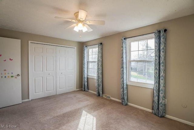 unfurnished bedroom featuring multiple windows, light colored carpet, ceiling fan, and a closet