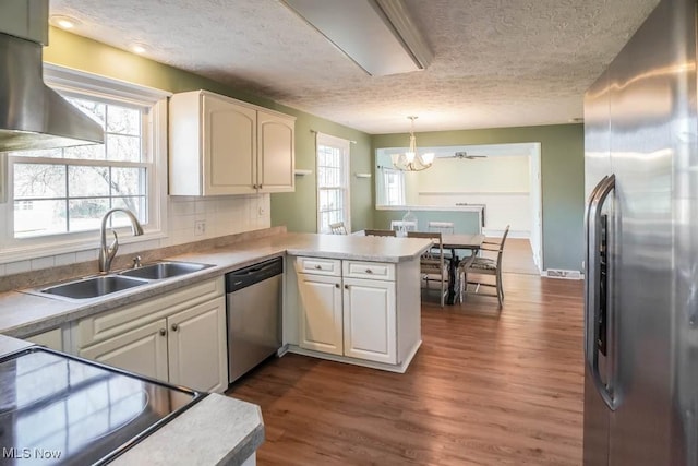 kitchen featuring sink, appliances with stainless steel finishes, dark hardwood / wood-style flooring, decorative light fixtures, and kitchen peninsula