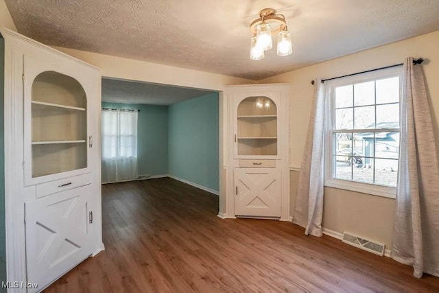 unfurnished dining area with dark wood-type flooring, built in features, and a textured ceiling