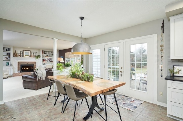 tiled dining space with french doors, built in features, decorative columns, and a brick fireplace