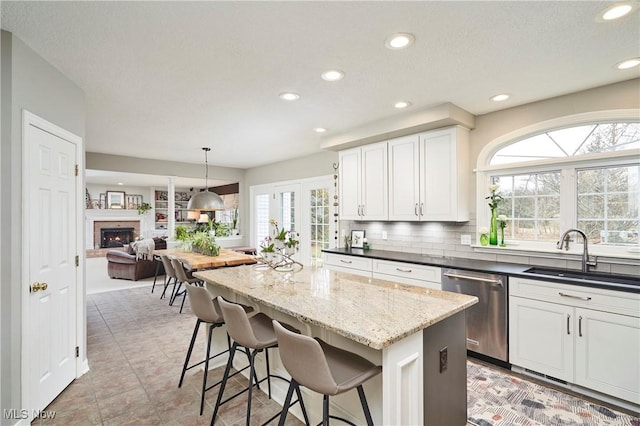 kitchen featuring sink, white cabinetry, a center island, stainless steel dishwasher, and pendant lighting