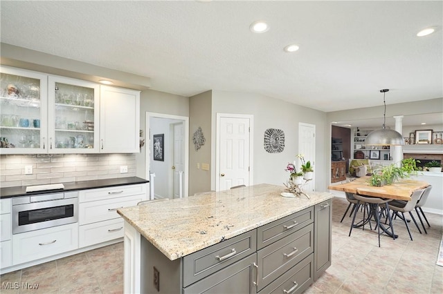 kitchen with gray cabinetry, white cabinetry, light stone counters, decorative light fixtures, and a kitchen island