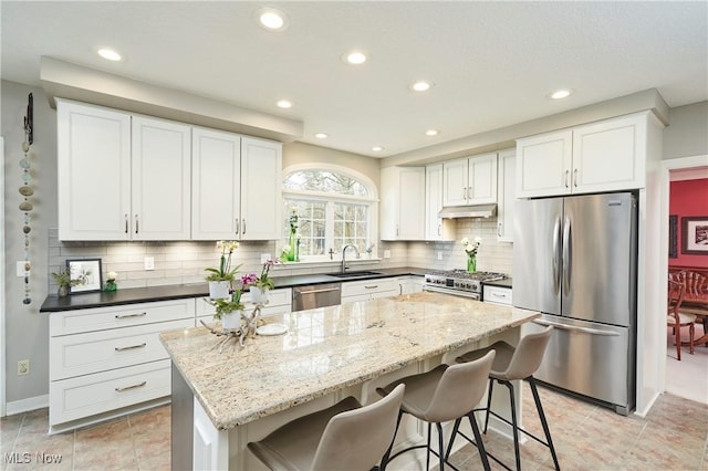 kitchen with appliances with stainless steel finishes, a center island, white cabinets, decorative backsplash, and dark stone counters