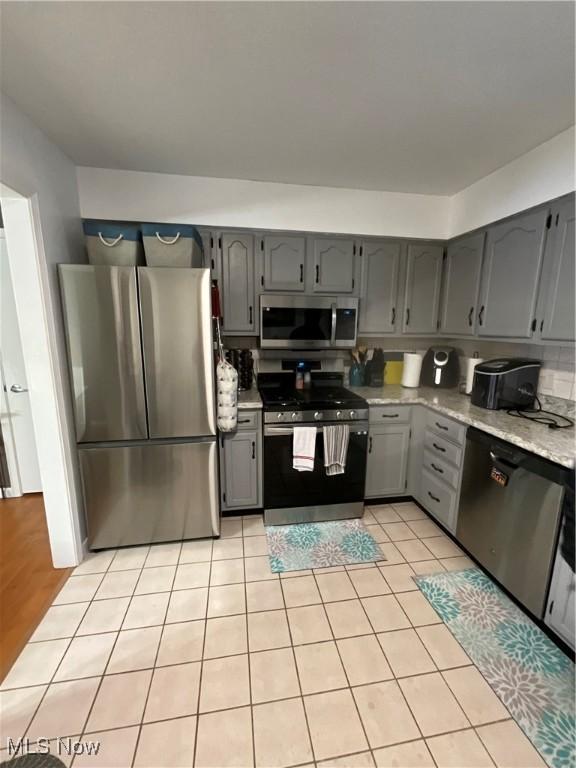 kitchen featuring stainless steel appliances, light stone countertops, gray cabinets, and light tile patterned floors