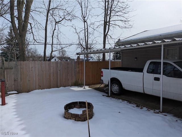 yard covered in snow with a carport and a fire pit