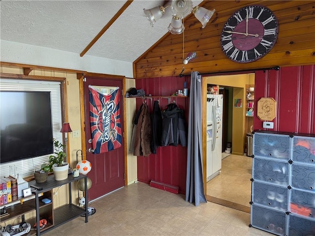 interior space with ceiling fan, lofted ceiling, a textured ceiling, and wood walls