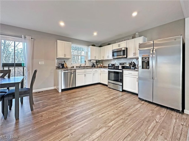 kitchen with sink, white cabinetry, appliances with stainless steel finishes, light hardwood / wood-style floors, and backsplash