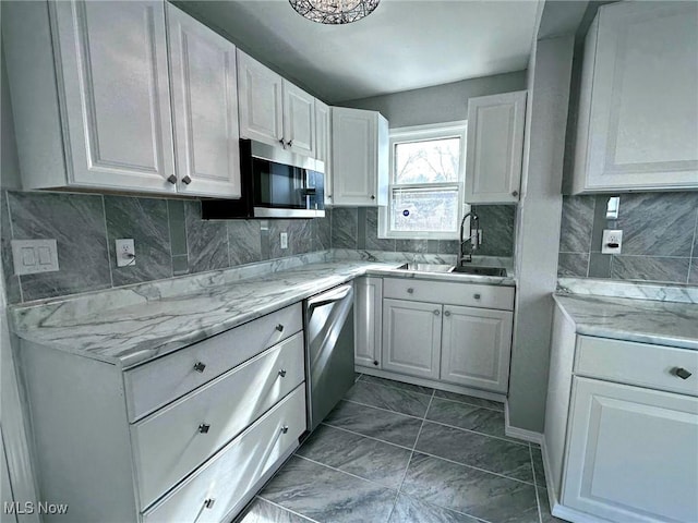 kitchen with sink, appliances with stainless steel finishes, white cabinetry, light stone countertops, and decorative backsplash