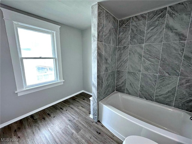 bathroom with tiled shower / bath combo, wood-type flooring, and toilet