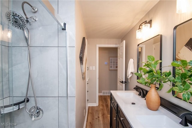 bathroom with wood-type flooring, tiled shower, and vanity