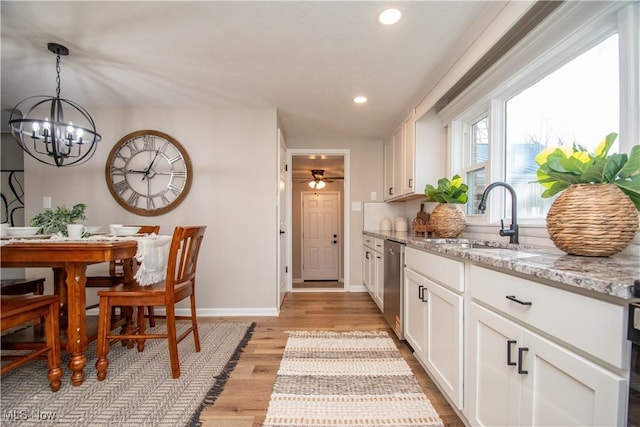 kitchen with sink, light hardwood / wood-style flooring, light stone counters, white cabinets, and stainless steel dishwasher