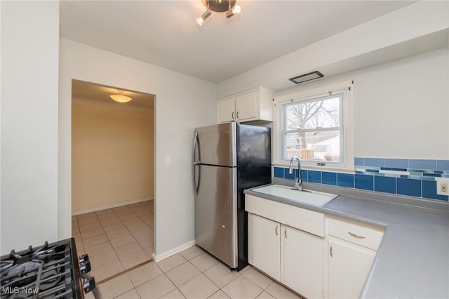 kitchen featuring sink, light tile patterned floors, stainless steel refrigerator, white cabinetry, and tasteful backsplash