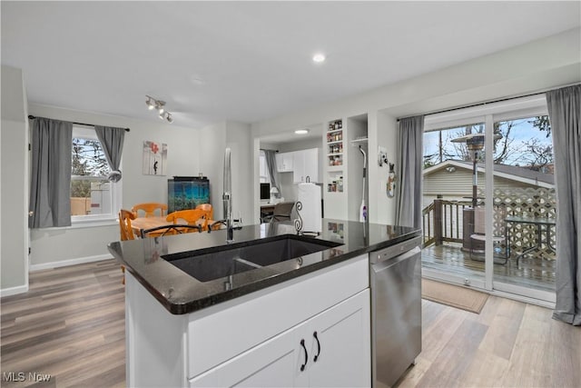 kitchen with white cabinetry, dishwasher, dark stone countertops, a kitchen island with sink, and light hardwood / wood-style flooring