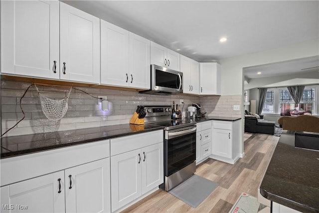 kitchen featuring appliances with stainless steel finishes, white cabinets, dark stone counters, light hardwood / wood-style floors, and backsplash