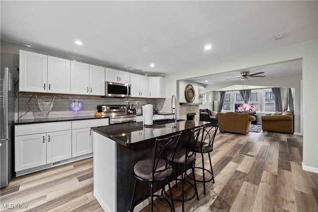 kitchen with light hardwood / wood-style flooring, appliances with stainless steel finishes, an island with sink, white cabinets, and a kitchen bar