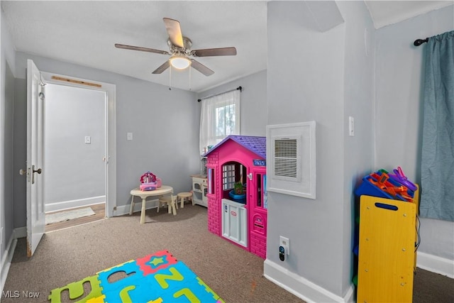 playroom with ceiling fan and dark colored carpet