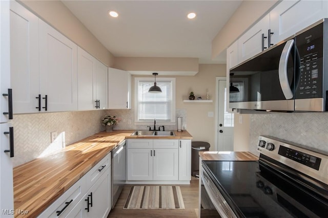 kitchen featuring stainless steel appliances, butcher block countertops, hanging light fixtures, and white cabinets