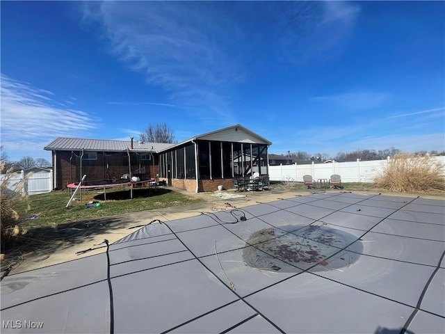 back of property featuring a trampoline, a patio, a covered pool, and a sunroom