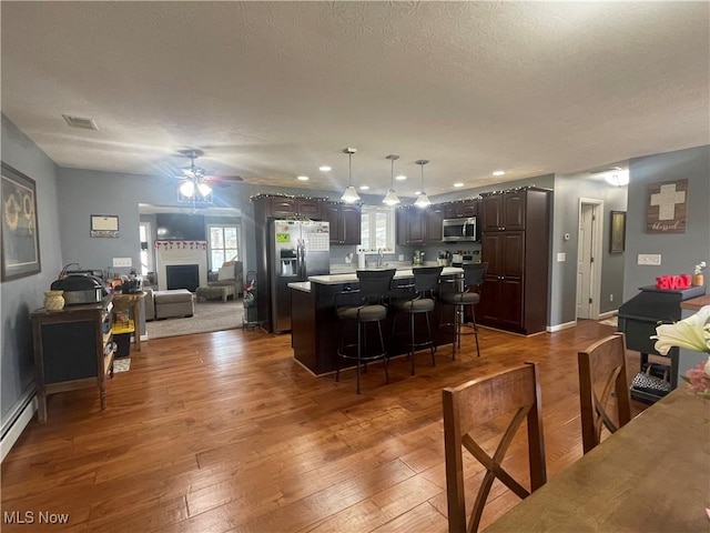 kitchen with appliances with stainless steel finishes, a breakfast bar, a center island, dark brown cabinetry, and dark wood-type flooring