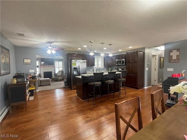 kitchen featuring dark wood-type flooring, appliances with stainless steel finishes, dark brown cabinets, a kitchen island, and a kitchen bar