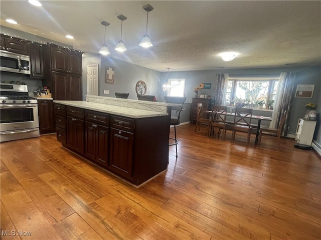 kitchen featuring a breakfast bar, dark brown cabinets, pendant lighting, stainless steel appliances, and hardwood / wood-style floors