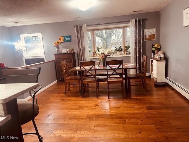 dining space with wood-type flooring, a chandelier, and baseboard heating