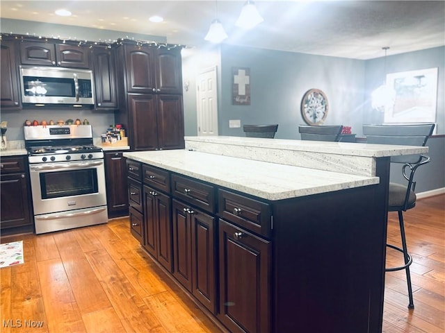 kitchen featuring a kitchen island, decorative light fixtures, a breakfast bar area, stainless steel appliances, and light hardwood / wood-style flooring