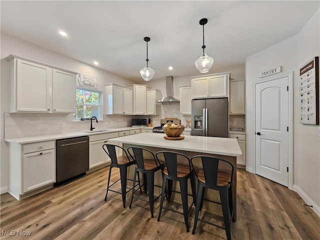 kitchen with wall chimney exhaust hood, sink, a center island, appliances with stainless steel finishes, and pendant lighting