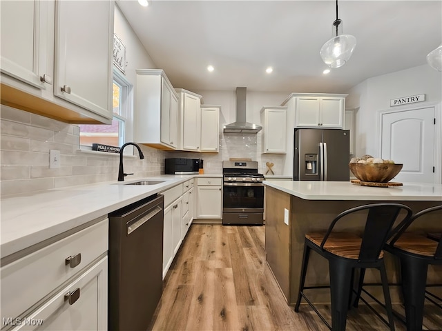 kitchen with white cabinets, a kitchen bar, hanging light fixtures, stainless steel appliances, and wall chimney exhaust hood