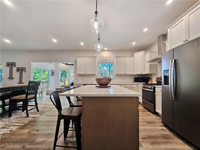 kitchen with wall chimney range hood, a breakfast bar, stainless steel appliances, white cabinets, and decorative light fixtures