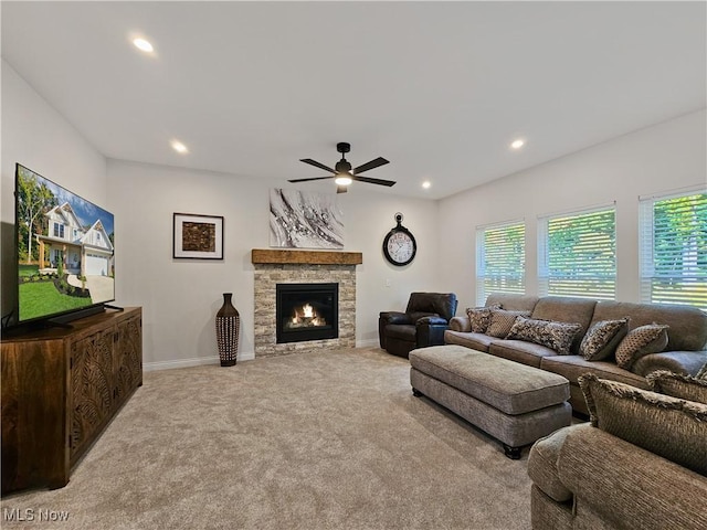 carpeted living room with ceiling fan, a healthy amount of sunlight, and a stone fireplace