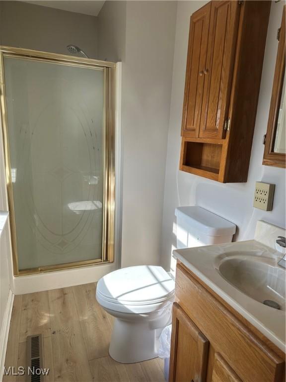 bathroom featuring wood-type flooring, vanity, an enclosed shower, and toilet