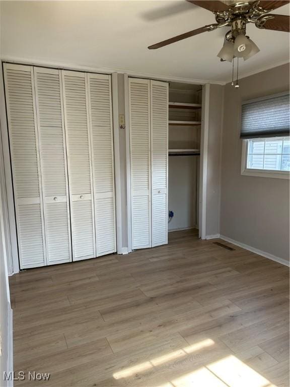 unfurnished bedroom featuring ceiling fan, ornamental molding, light hardwood / wood-style floors, and two closets