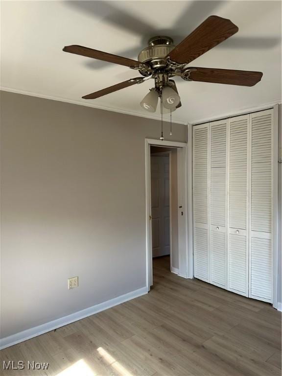 unfurnished bedroom featuring crown molding, hardwood / wood-style floors, ceiling fan, and a closet