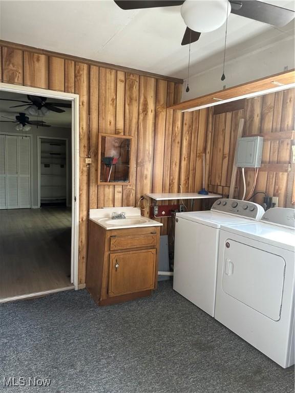 laundry area featuring sink, ceiling fan, washing machine and dryer, cabinets, and wood walls