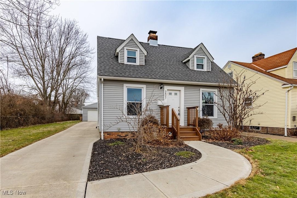 new england style home with a garage, an outdoor structure, and a front lawn