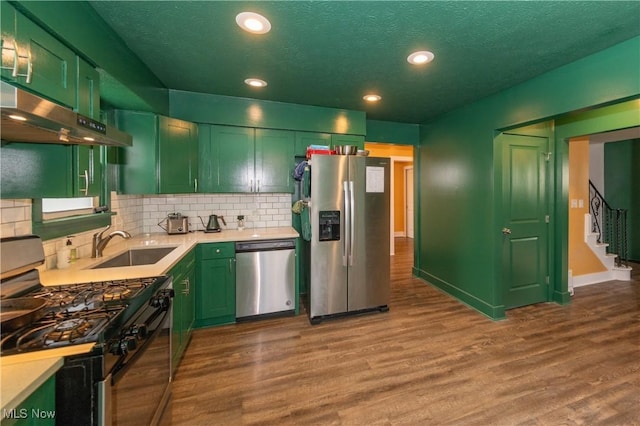 kitchen with decorative backsplash, stainless steel appliances, green cabinets, and hardwood / wood-style floors