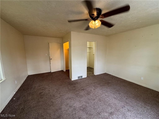 unfurnished bedroom with dark carpet, a textured ceiling, ceiling fan, and a spacious closet