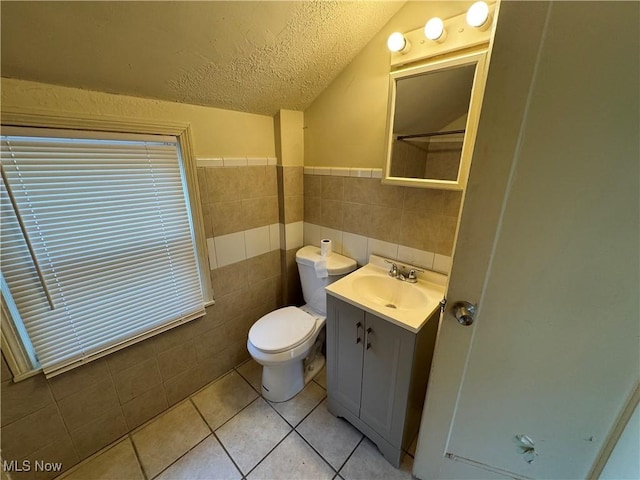 bathroom featuring tile walls, vanity, a textured ceiling, vaulted ceiling, and tile patterned floors