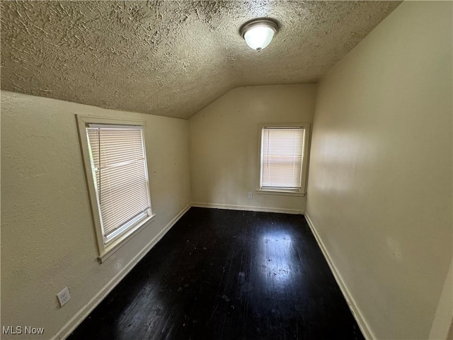 additional living space featuring dark hardwood / wood-style flooring, vaulted ceiling, and a textured ceiling