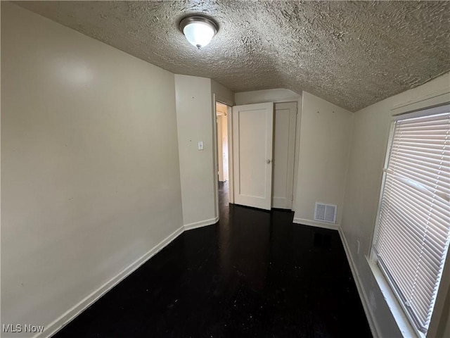 unfurnished room featuring vaulted ceiling and a textured ceiling